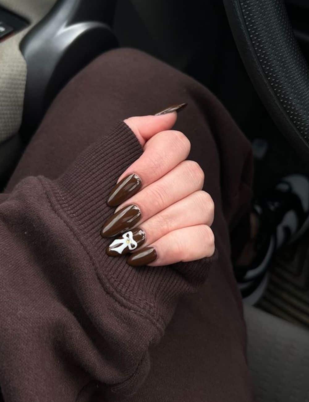 long chocolate brown almond nails with a white bow accent nail